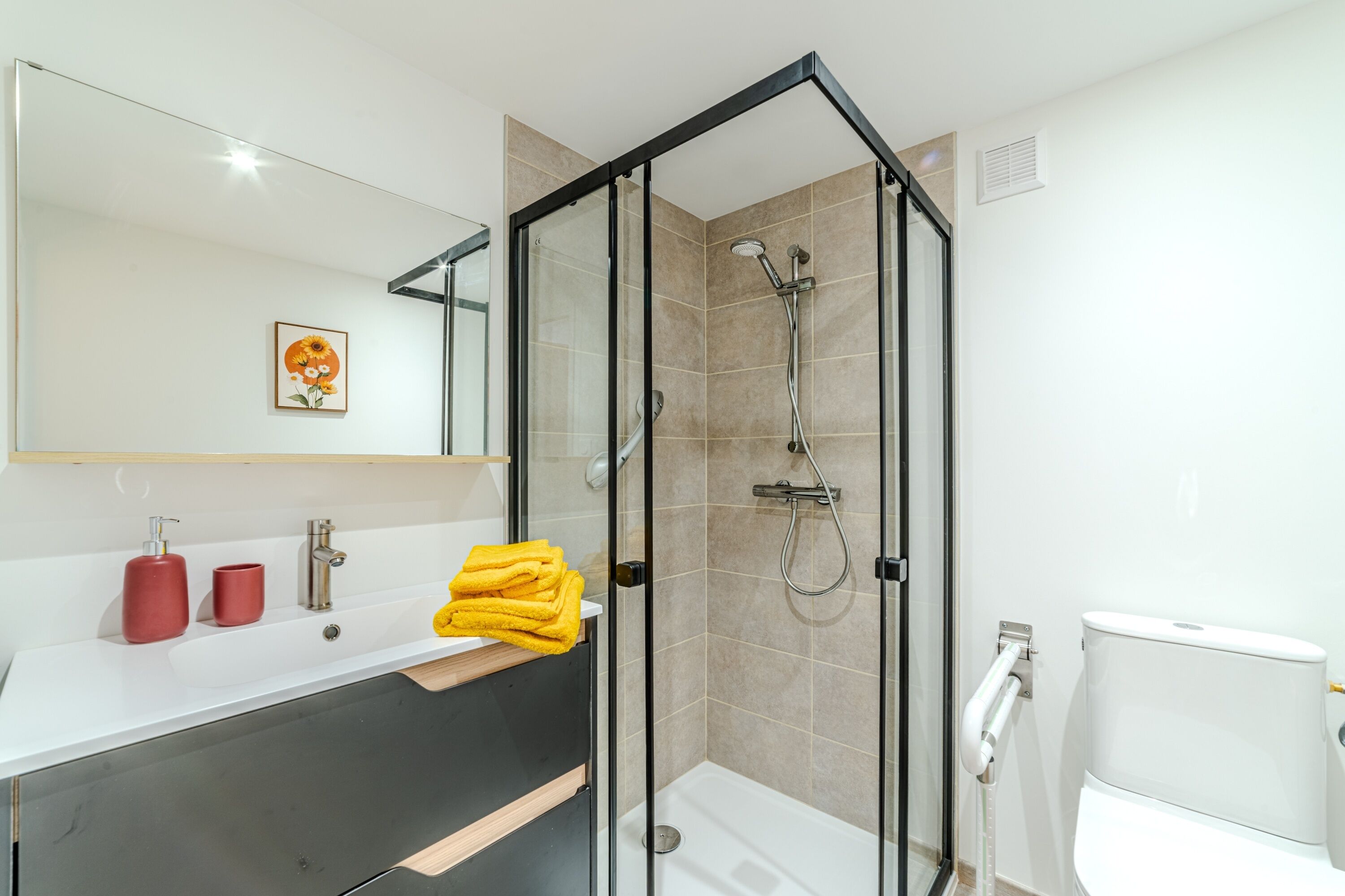 Ein modernes Badezimmer mit einer gläsernen Duschkabine, einem weißen Waschbecken und roten Seifenspendern sowie einer Toilette.