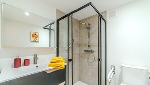 Un baño moderno con cabina de ducha de vidrio, un lavamanos blanco y dispensadores de jabón rojos, y un inodoro.