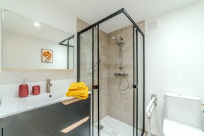 Ein modernes Badezimmer mit einer gläsernen Duschkabine, einem weißen Waschbecken und roten Seifenspendern sowie einer Toilette.