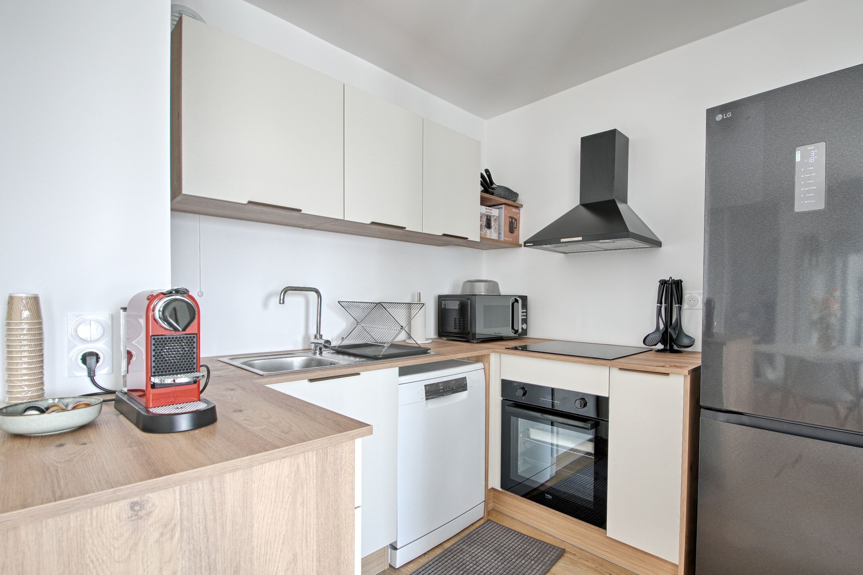 A compact kitchen with white cabinets, a stainless steel refrigerator, a microwave, a dishwasher, and a coffee machine.