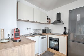 Una cocina compacta con armarios blancos, un refrigerador de acero inoxidable, microondas, lavavajillas y cafetera.