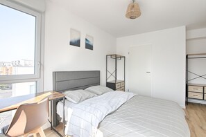 Un dormitorio moderno con cama, escritorio y silla. Una ventana ofrece vistas al exterior.