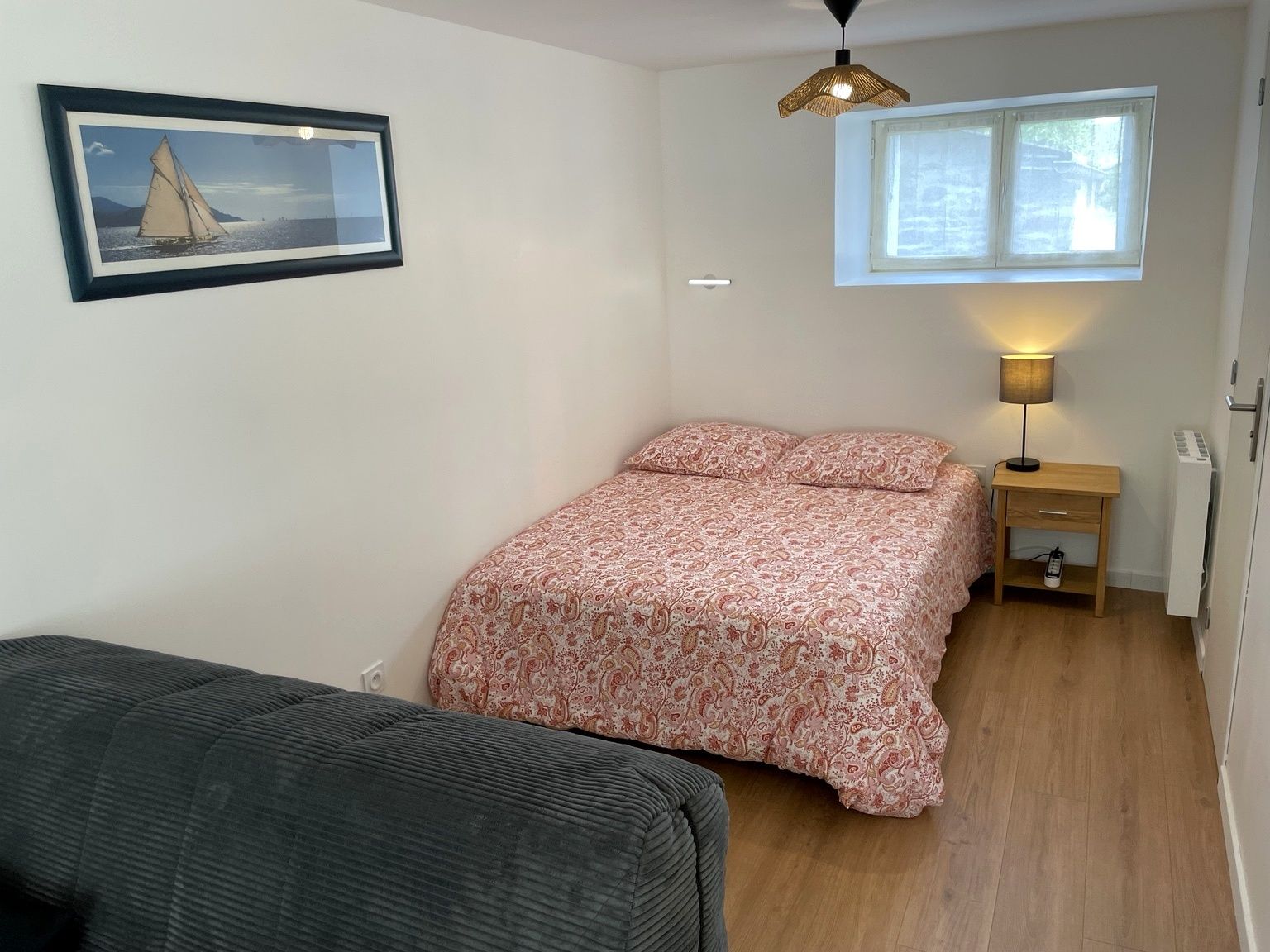 A bedroom with a bed, a nightstand, a lamp, a window, and a framed picture on the wall.