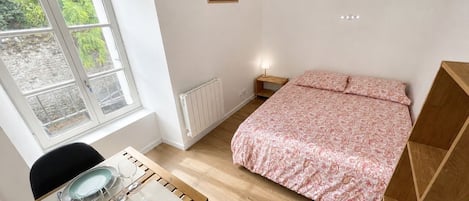 Makuuhuone, jossa on sänky, ikkuna, yöpöytä ja ruokailuvälineillä varustettu pöytä.