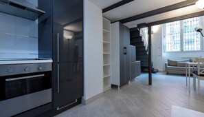 A modern kitchen with built-in appliances, a staircase leading to a balcony, and a dining area with a table and chairs.