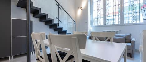 A modern interior with a staircase, white furniture, and a view through a window with decorative bars.
