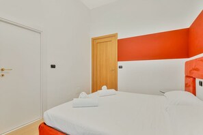 Ein Hotelzimmer mit einem Einzelbett, einer Holztür und einer leuchtend orangefarbenen Akzentwand.