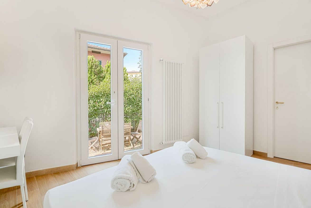 A hotel room with a bed, a chair, a wardrobe, and a sliding glass door leading to an outdoor area.