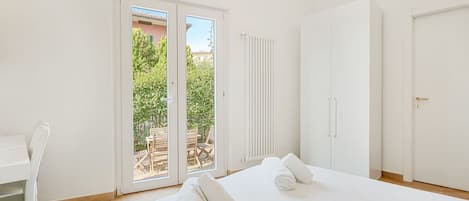 Habitación de hotel con cama, una silla, armario y puerta corredera de vidrio que da a un espacio exterior.