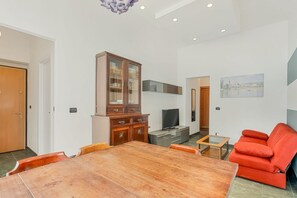 Ein modernes Wohnzimmer mit Esstisch, rotem Sofa, Fernseher und Schrank.