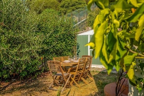A wooden table and chairs set outdoors, surrounded by dense greenery and a green building in the background. - [Val Zagora] 5Terre-Private parking (La Spezia)