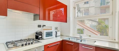 A kitchen with a gas stove, microwave, and a window with a view of buildings.