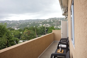 Ein Balkon mit Tisch und Stühlen, der einen Blick auf eine Hügellandschaft mit Gebäuden bietet.