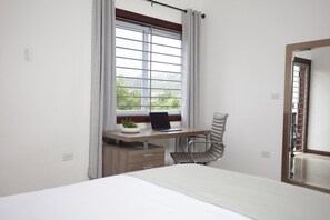 Ein Schlafzimmer mit einem Bett, einem Schreibtisch mit Laptop, einem Stuhl und einem Fenster mit Vorhängen.