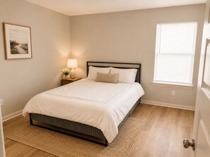 Een slaapkamer met een bed, nachtkastje, lamp en een raam.