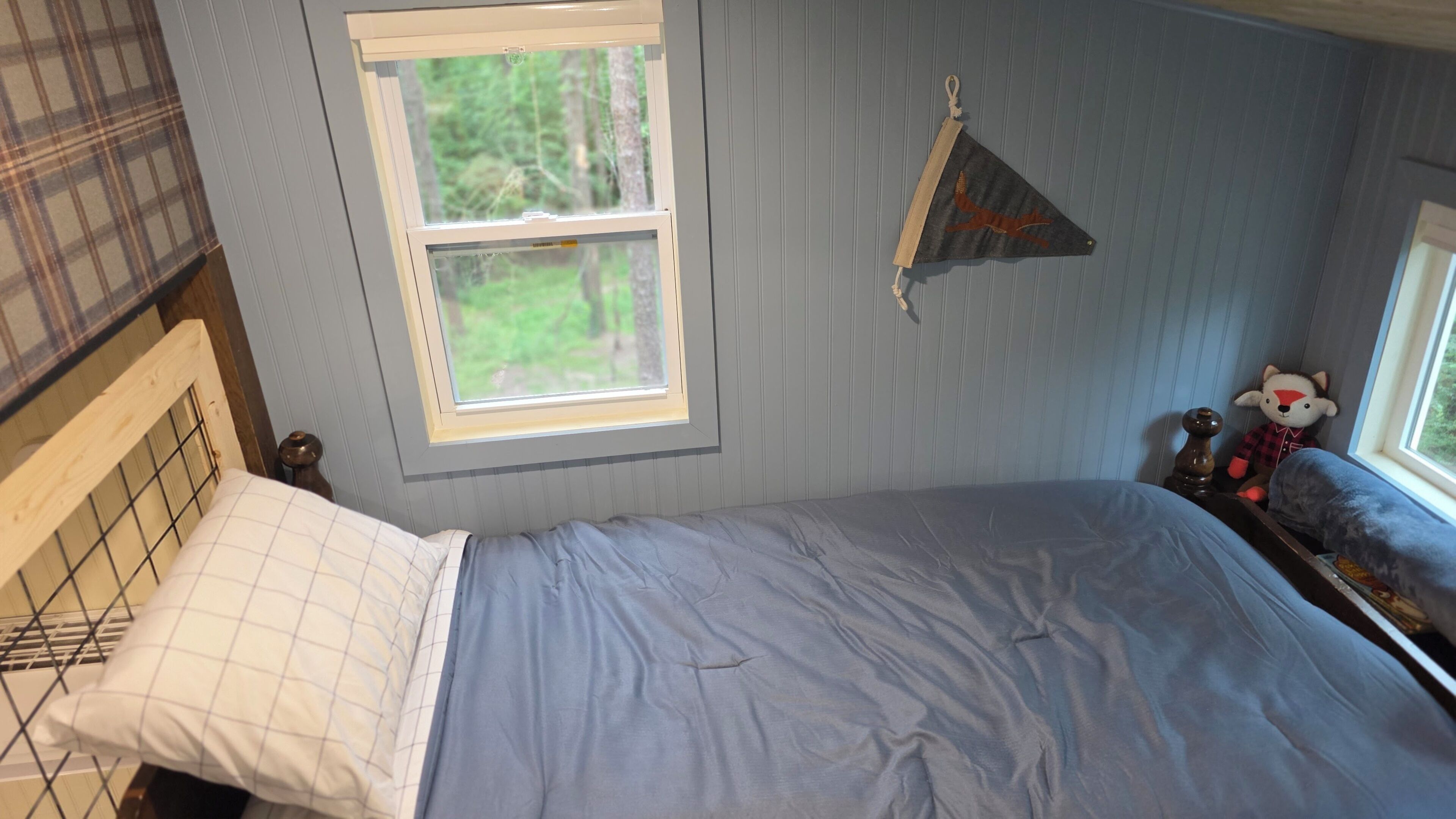 A bedroom with a single bed, a window, a wall-mounted flag, and a stuffed toy.