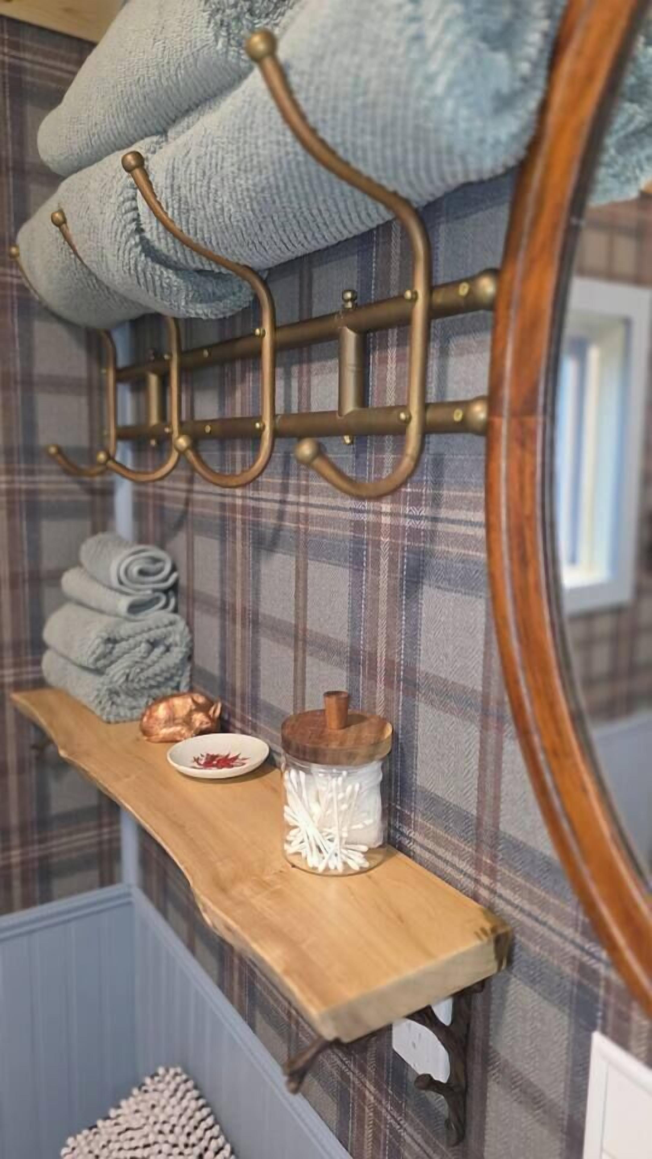 A bathroom with a wooden shelf holding towels, a copper pot, and a glass jar.