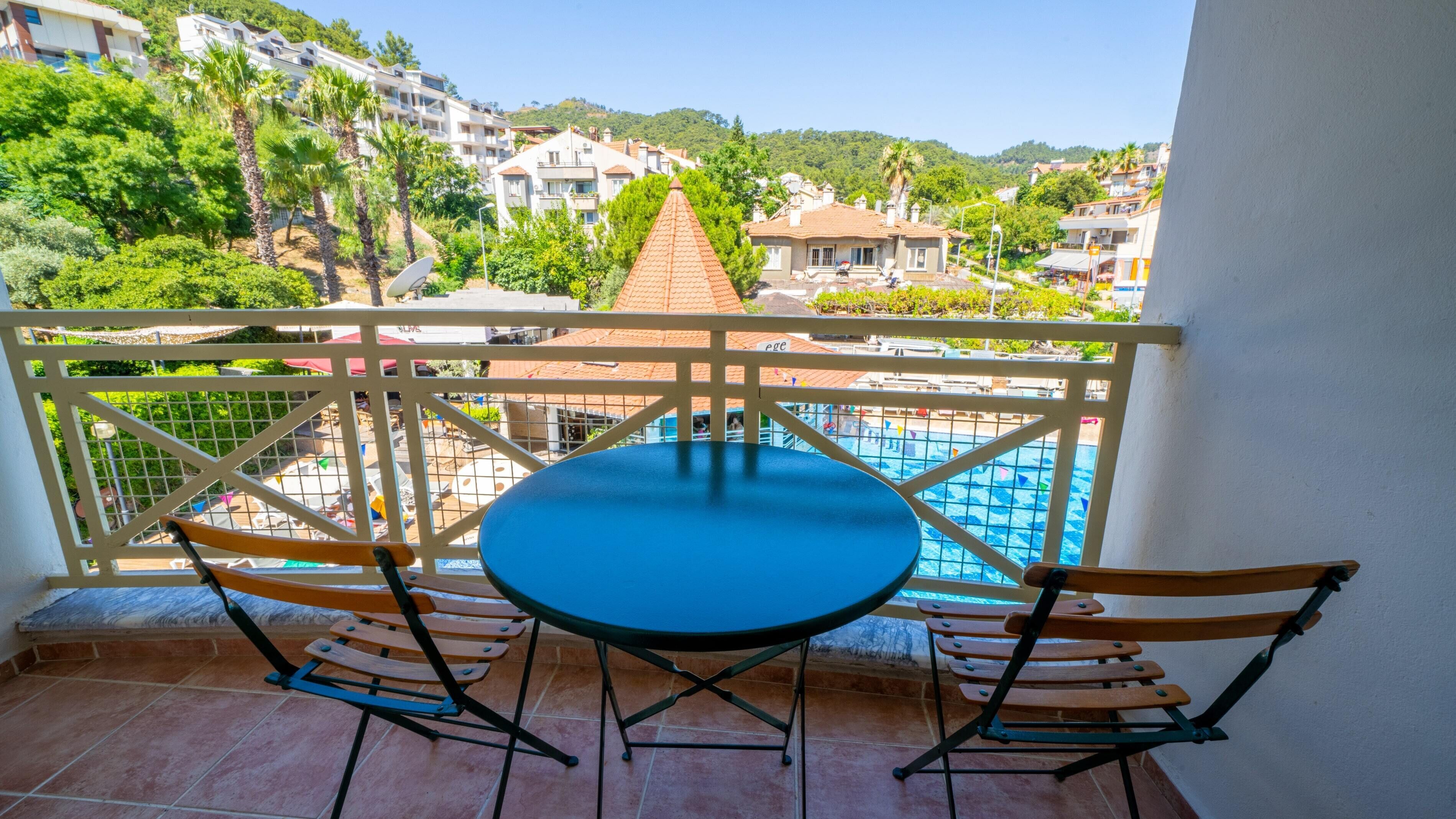 Un balcón con mesa y sillas, con vista a una piscina y edificios residenciales.