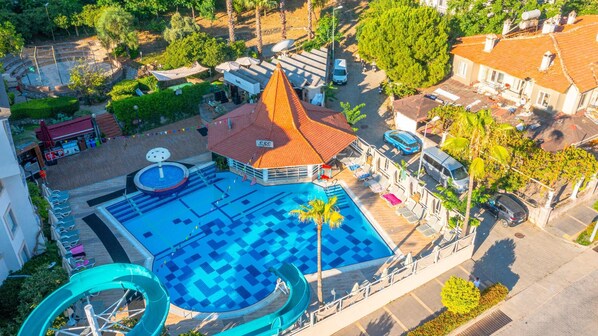 An aerial view of a resort with a swimming pool, a water slide, and a small building with a red roof.