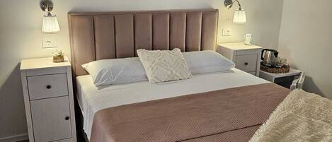 Quarto de hotel com uma cama grande, duas mesas de cabeceira, um criado-mudo, um painel decorativo e um tapete.