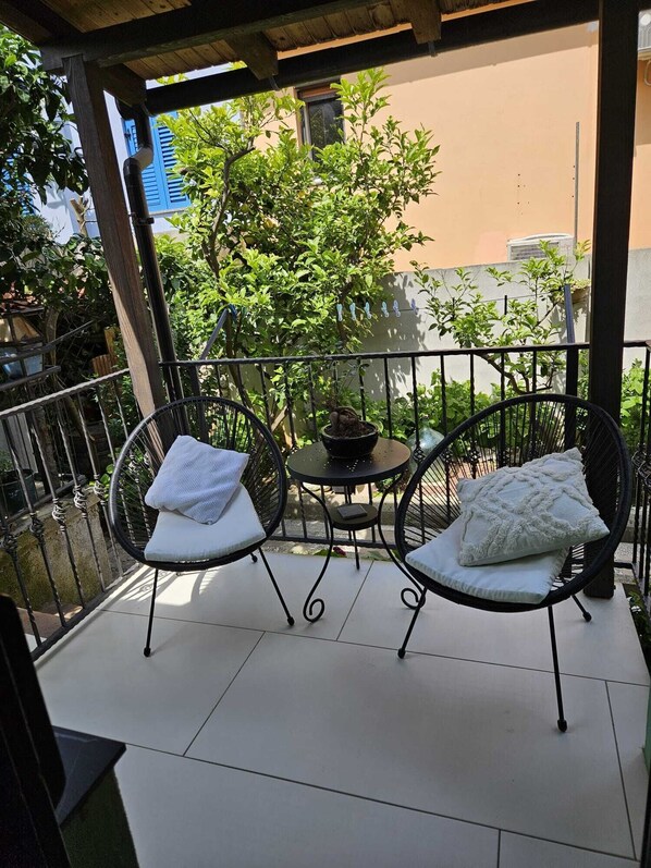 A balcony with two wicker chairs and a small round table, surrounded by a metal railing.