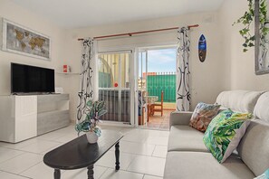 A living room with a television, a sofa, a coffee table, and a sliding glass door leading to an outdoor area. - Vacation Apartment 'Vacanze Mareverde' with Mountain View, Shared Pool and Wi-Fi (Costa Adeje)
