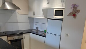 Moderni keittiö, jossa on valkoiset kaapit, musta työtaso ja ruostumattomasta teräksestä valmistetut kodinkoneet.