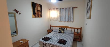 Un dormitorio con cama, mesita de noche, espejo y un cuadro colgado en la pared.