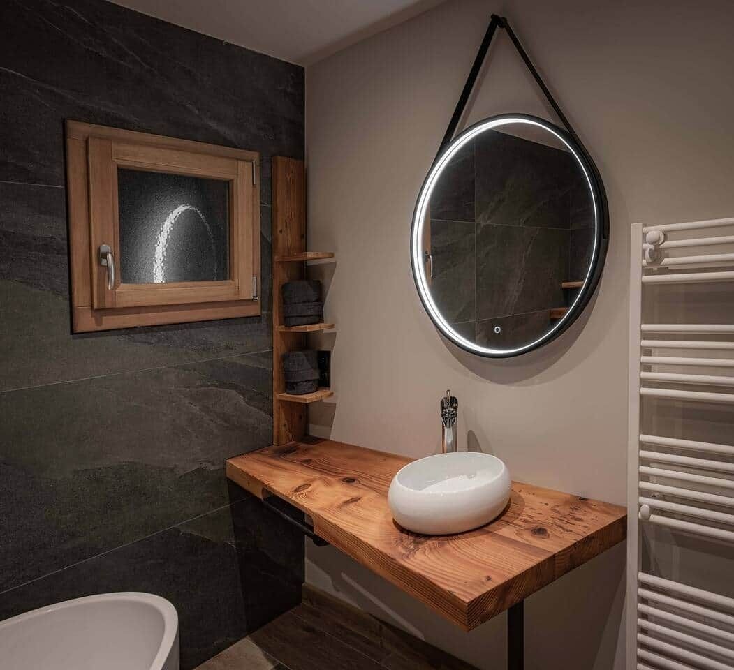 Ein modernes Badezimmer mit einem Holzschrank, einem runden Spiegel und einer eingebauten Ablagefläche.