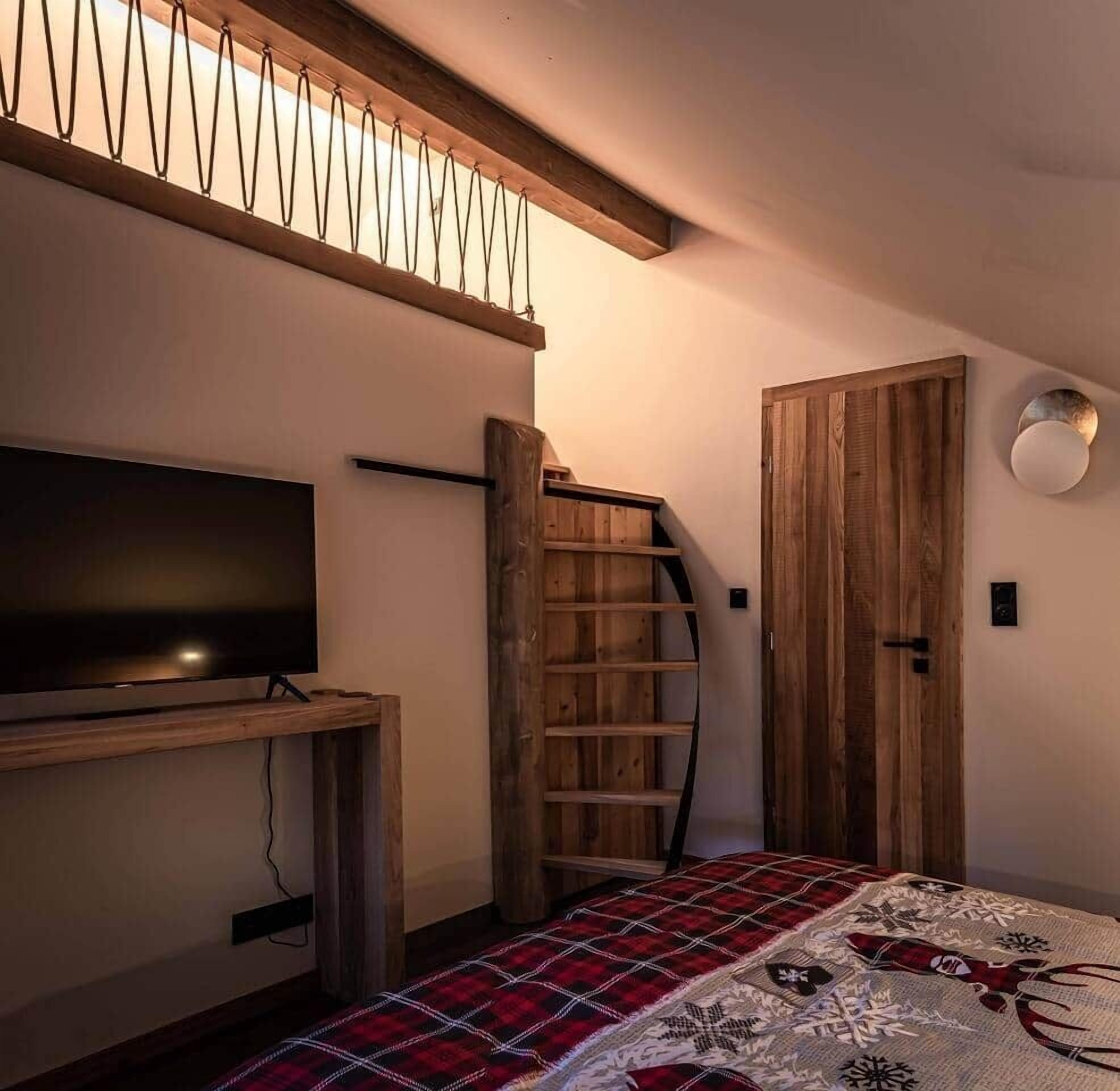 A bedroom with a television, a wooden ladder, a door, and a patterned bedspread.