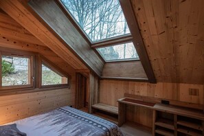 Ein Holzinnenraum mit schrägen Wänden, Oberlichtern, einem Bett und einer Bank.