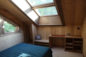 Ein Zimmer mit schrägem Dach, Dachfenstern, einem Bett, einem Schreibtisch und einer Bank.