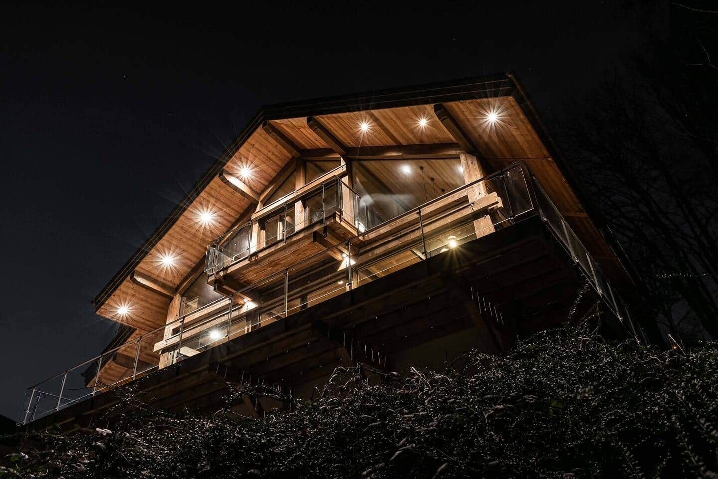 A multi-level wooden cabin with balconies, illuminated by exterior lights.