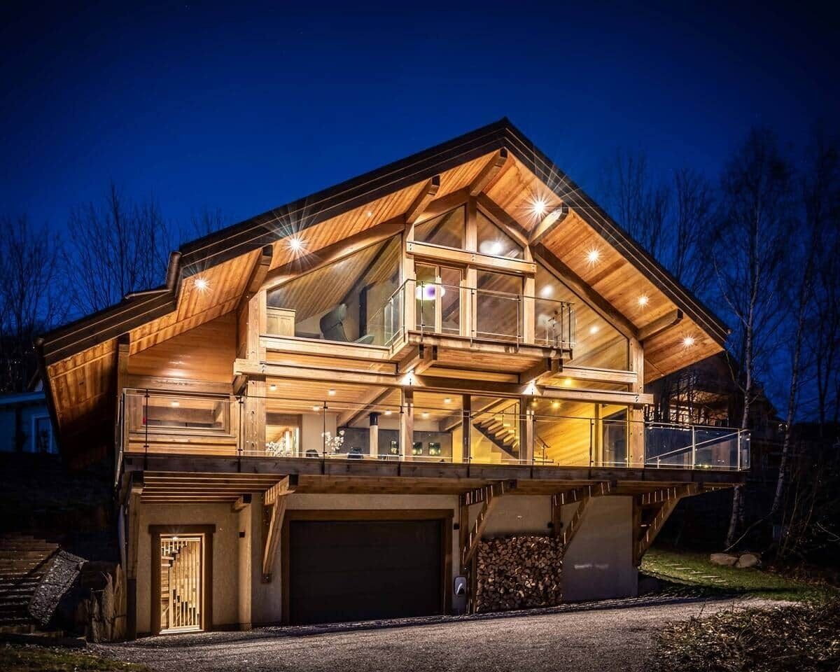 A multi-level wooden house with a garage, large windows, and a balcony.