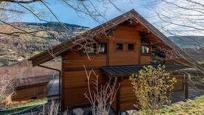 Eine Holzhütte mit geneigtem Dach, einer kleinen Veranda und Blick auf eine gebirgige Landschaft.