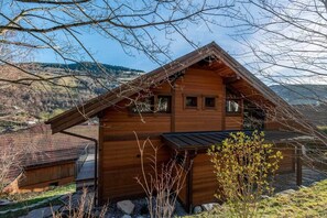 Eine Holzhütte mit geneigtem Dach, einer kleinen Veranda und Blick auf eine gebirgige Landschaft.