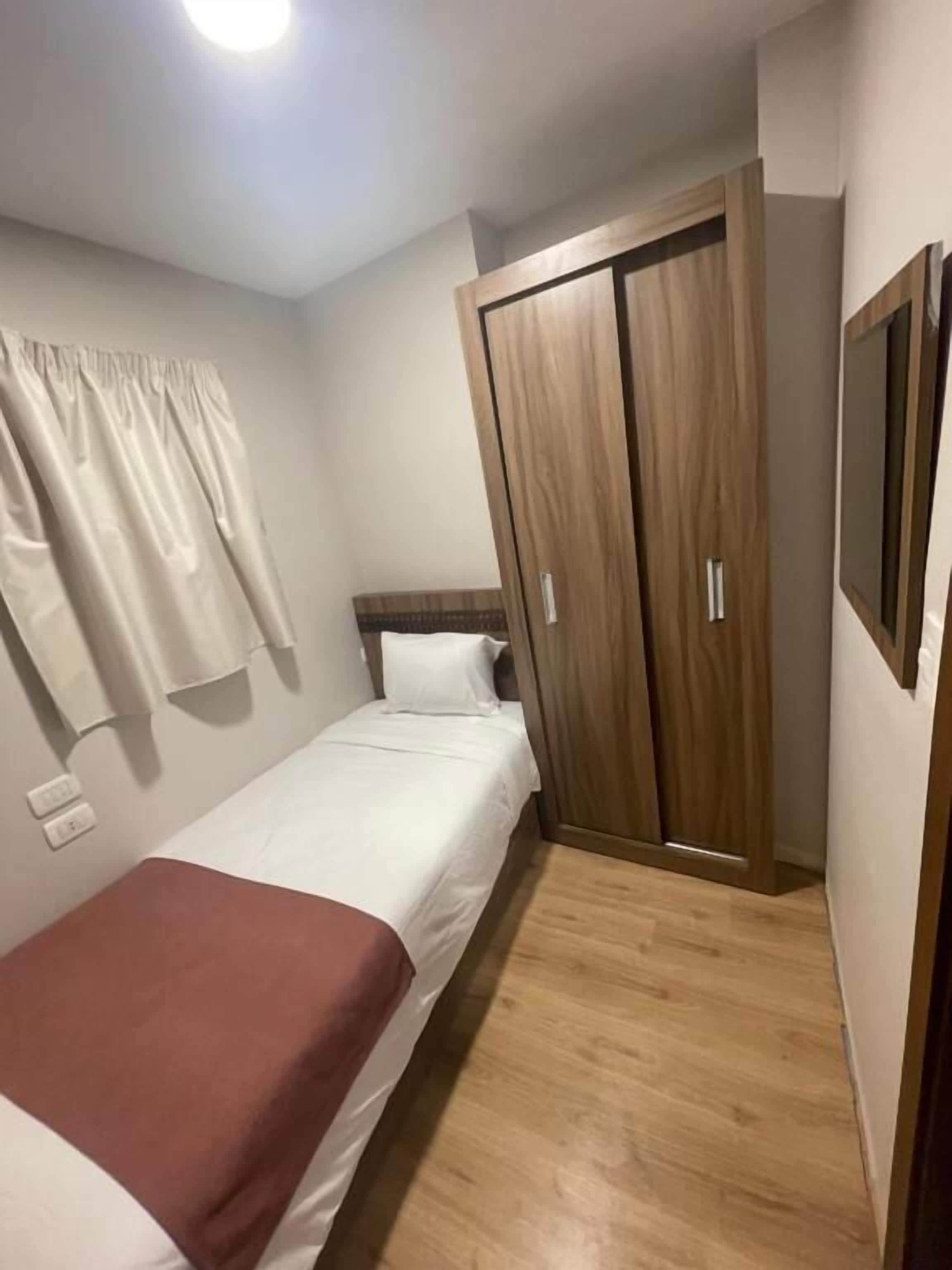 A bedroom with a single bed, a wooden wardrobe, a television, and a curtain.