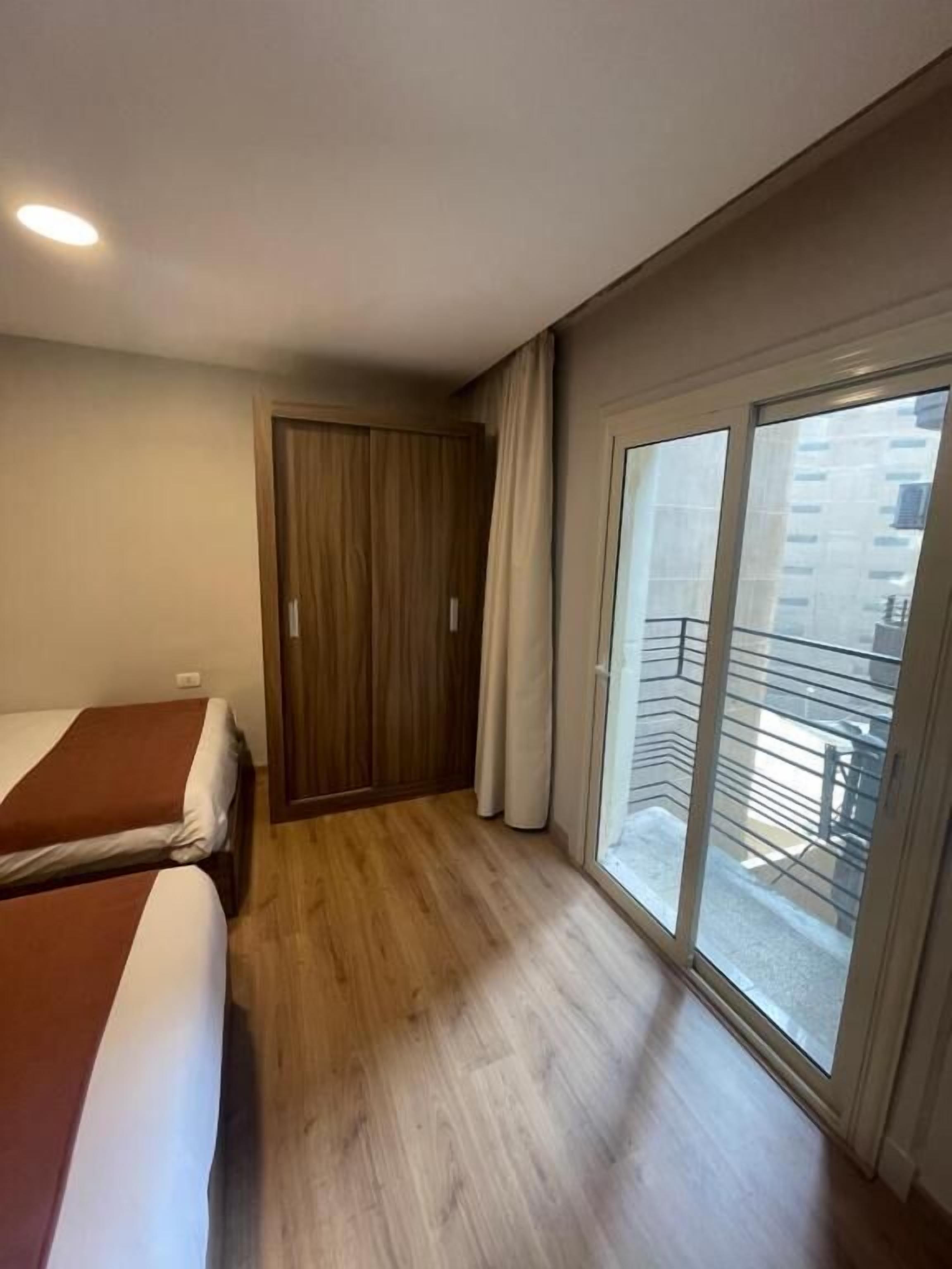 Habitación de hotel con dos camas, un armario de madera y un balcón con vistas a la ciudad.