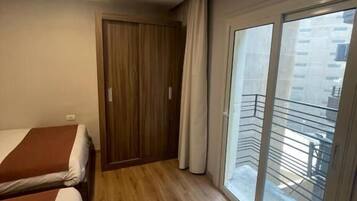 Habitación de hotel con dos camas, un armario de madera y un balcón con vistas a la ciudad.