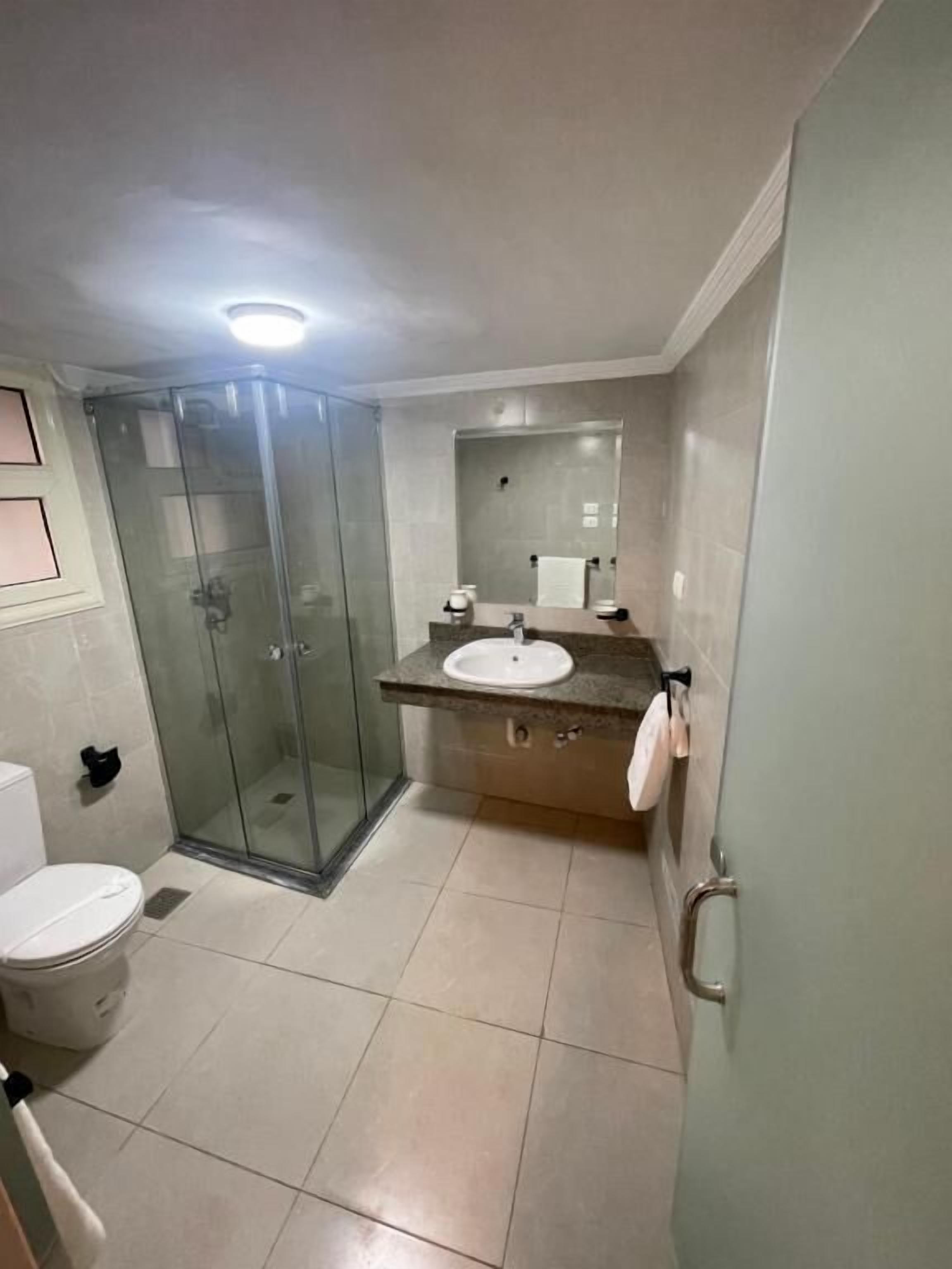 Un baño con ducha de vidrio, inodoro y lavamanos con espejo.