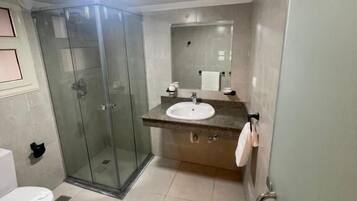 Un baño con ducha de vidrio, inodoro y lavamanos con espejo.