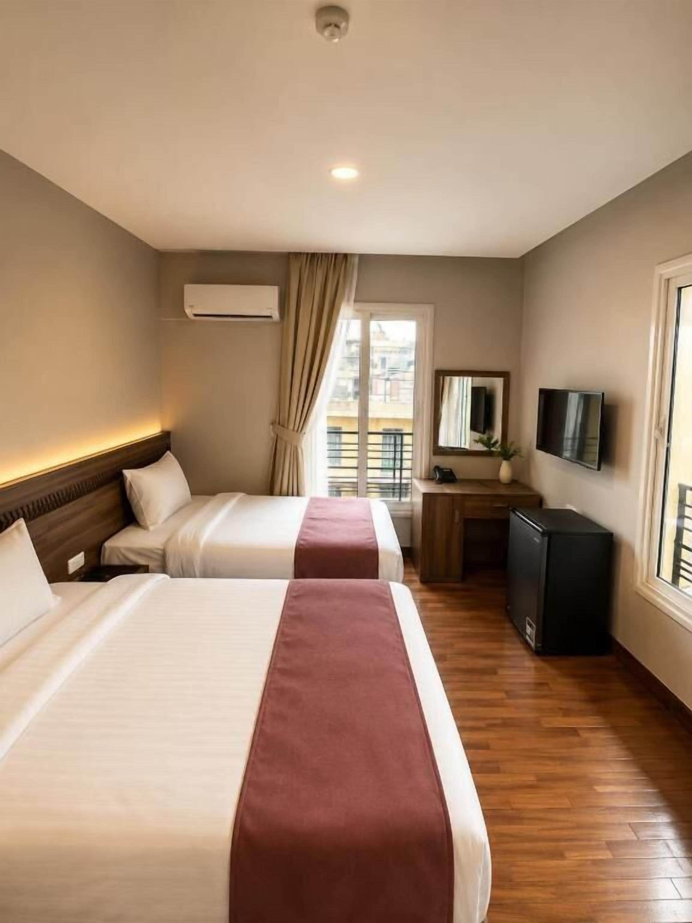 Una habitación de hotel con dos camas, televisión, escritorio y ventana con cortinas.