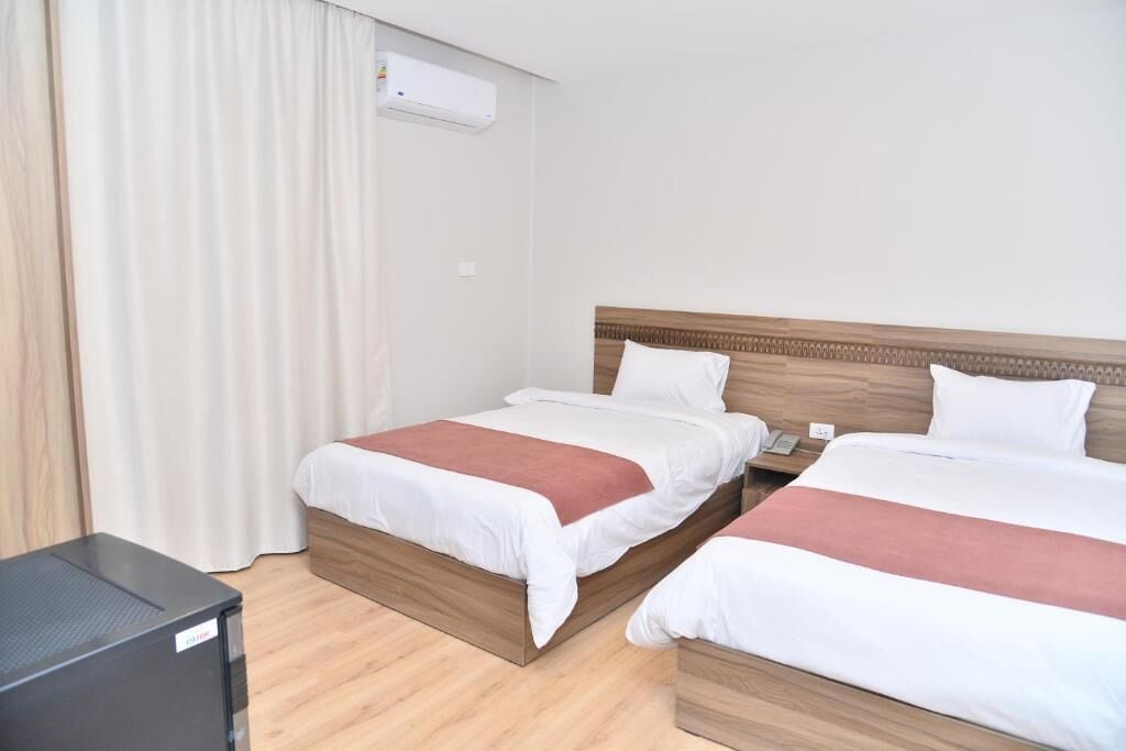 Habitación de hotel con dos camas, cabecera de madera, mesita de noche y televisor de pantalla plana.