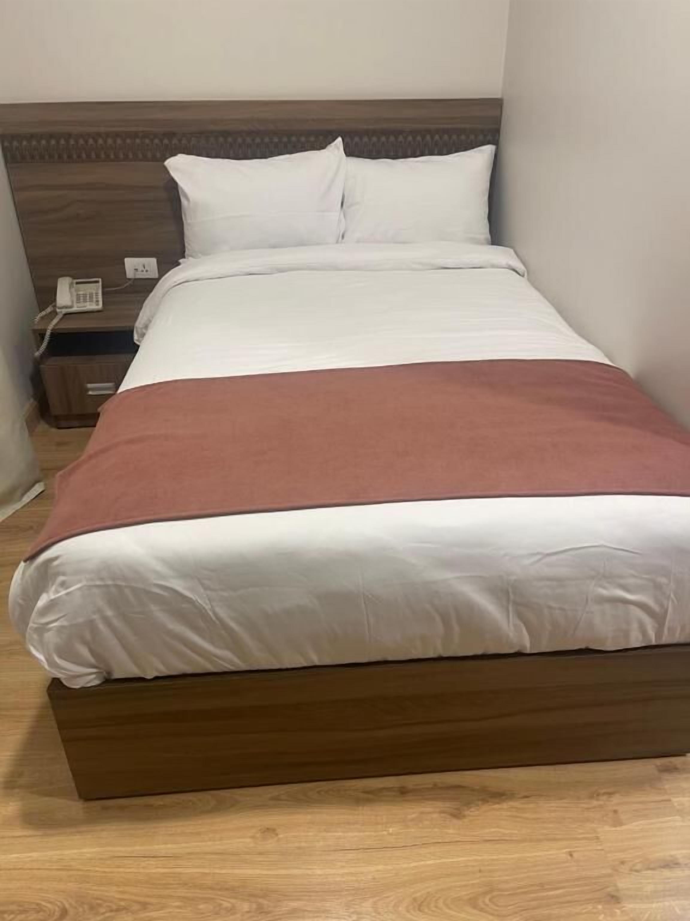 Una cama individual con cabecera de madera, ropa de cama blanca y una manta marrón.
