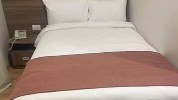 Una cama individual con cabecera de madera, ropa de cama blanca y una manta marrón.