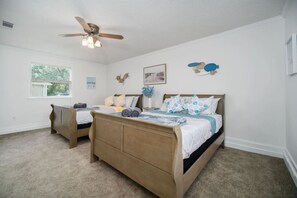 Une chambre à coucher comprenant un lit, une table de chevet, une commode, un ventilateur de plafond et une fenêtre avec des stores.