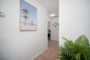 A hallway with a framed beach scene, a potted plant, and a door leading to another room. - Bright Horizons Hideaway w/POOL- 18 min to MAYO (Jacksonville)