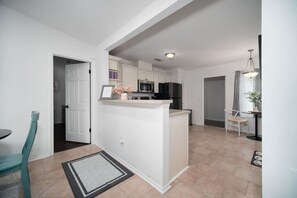 A modern kitchen with white cabinetry, a central island, and a dining area with a chair and table. - Bright Horizons Hideaway w/POOL- 18 min to MAYO (Jacksonville)