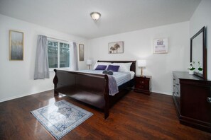 A bedroom with a wooden bed, a nightstand, a dresser, and a window with curtains. - Bright Horizons Hideaway w/POOL- 18 min to MAYO (Jacksonville)