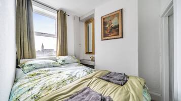 A hotel room with a bed, a window with curtains, a painting on the wall, and a door.